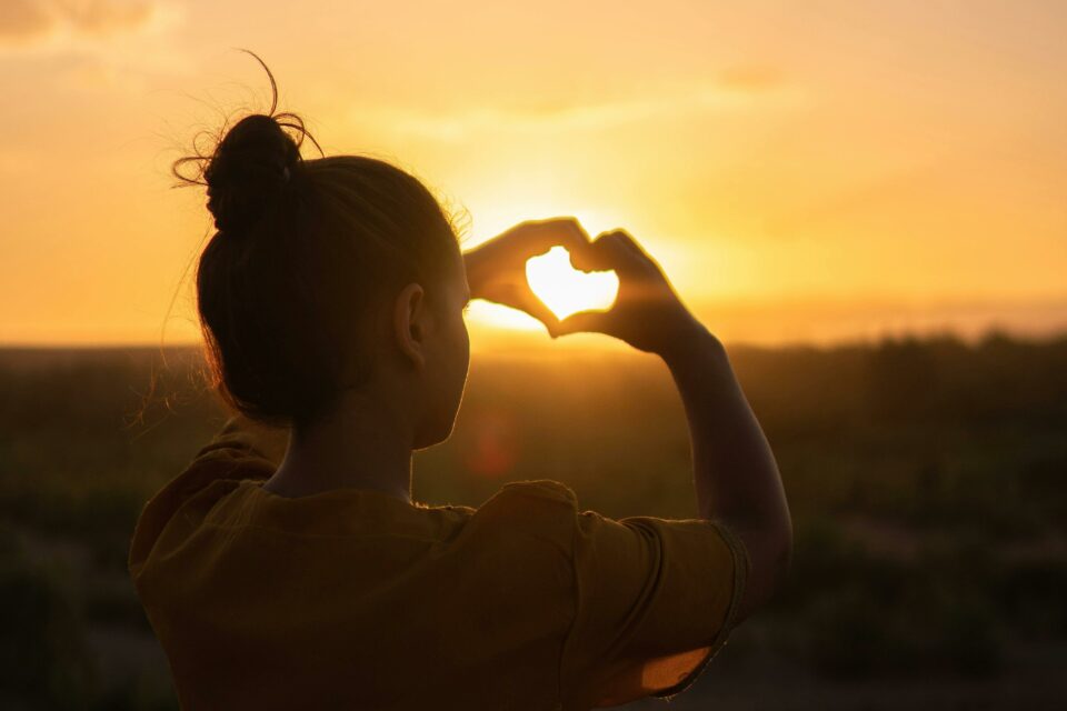 mujer joven hace forma corazón con las manos al aterdecer